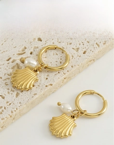 Détail macro de boucles d'oreilles en acier doré avec pendentifs coquillage et perle