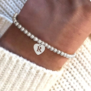 Silver beaded bracelet with heart pendant engraved letter R on model with sweater