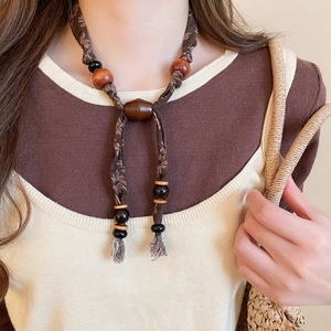Détail d'un collier bohème avec corde en tissu marron, perles en bois et glands fins