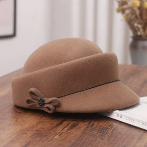 Detail of wool equestrian hat featuring a side bow with black beadwork on wood surface