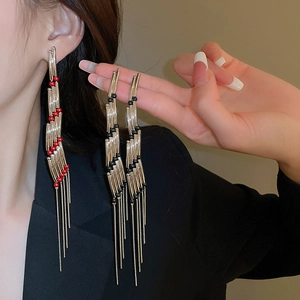 Detail of gold layered tassel earrings with red and black beads on a model