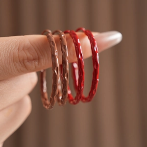 Detail of four hammered texture hoop earrings in brown and red held by a hand