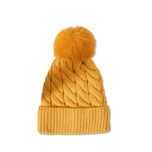 Close-up of yellow knit beanie featuring thick cable patterns and a large soft faux fur pom