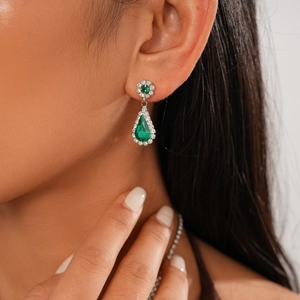 Close-up of vintage silver earrings featuring emerald green teardrop gems and diamonds