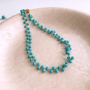 Détail de perles facettées turquoise et chaîne en métal doré sur un plateau céramique