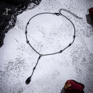 Detail of gothic Y-shaped necklace with black teardrop pendant and withered red rose