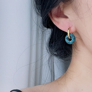 Close-up of gold hoop earring featuring a marbled blue stone pendant on a model