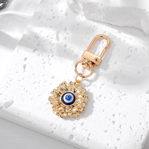 Close-up of golden flower keychain with blue evil eye bead on white stone