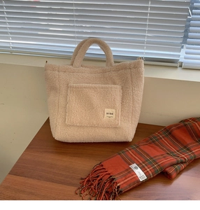 Detail of plush beige faux shearling tote bag with BYBR label on dark wood table