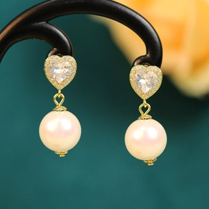 Close-up of elegant gold heart earrings with sparkling zircons and white round pearls