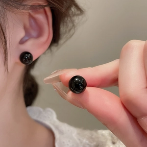 Close-up of minimalist black round stud earring worn on ear with high-gloss finish