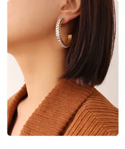 Close-up of golden C-shaped hoop earrings with baguette-cut zircon stones on model