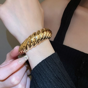 Close-up of golden croissant-style twisted bangle with high-polish metallic finish