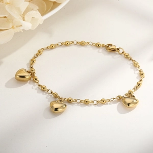 Close-up of gold heart pendant bracelet with bead and link chain on a neutral background