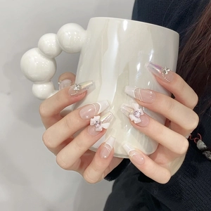 Macro shot of long trapezoid fake nails with French tips, 3D bows, and pearl accents
