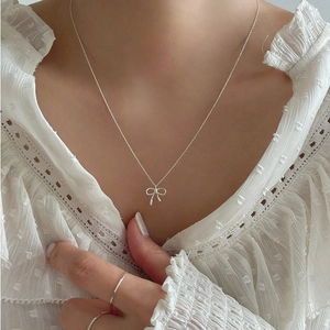 Detail of silver bow pendant necklace and minimalist rings on a model in white chiffon
