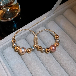 Close-up of twisted hoop earrings with gold, silver and purple metallic beads in a box
