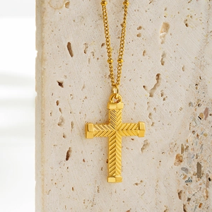 Detailed macro view of golden cross pendant with V-shaped engraving on beige stone