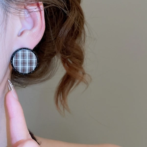 Macro detail of round brown checkered fabric stud earrings with elegant black circular frame