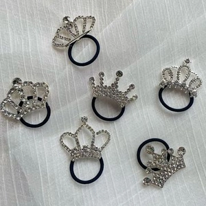 Detail of six silver crown hair ties with white rhinestones on white fabric