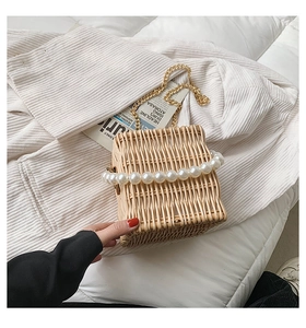 Detailed shot of handmade straw bag with pearl handle and gold chain on soft white fabric