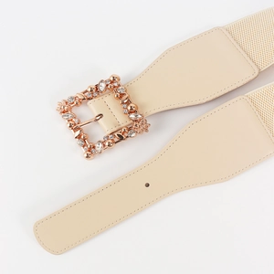 Close-up of beige elastic belt with ornate gold square buckle featuring rhinestones