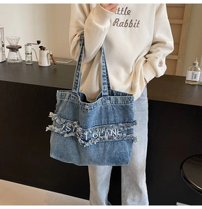 Détail du sac cabas en jean bleu avec lettrage blanc et finitions effilochées à franges