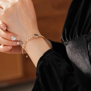 Dettaglio del bracciale aperto in oro con fiore in zircone e occhio azzurro intarsiato