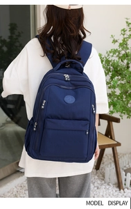 Close-up of a navy blue water-resistant nylon backpack worn by a model in outdoor setting