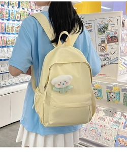 Detail of light yellow nylon backpack with a cute bear plush pendant worn by a model