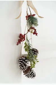Christmas wall hanging with pine cones, red berries, and a golden bell on white wall