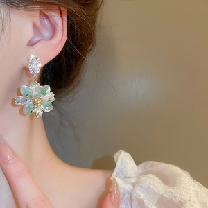 Close-up of green crystal flower earrings worn with elegant white lace clothing