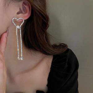 Détail de boucles d'oreilles cœur en argent avec de longs pompons et des strass blancs