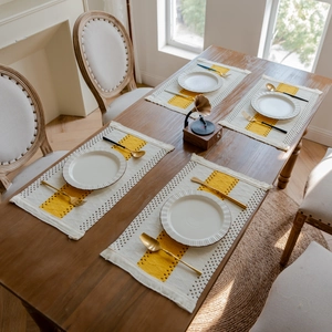 Close-up of woven linen table mat with yellow beige stitching and decorative tassels