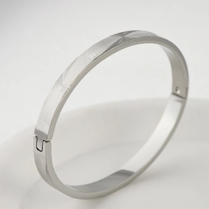 Macro detail of silver stainless steel bangle with crown logo and geometric mesh pattern