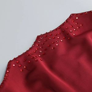 Détail macro du tissu satiné bordeaux avec strass carrés rouges décoratifs sur l'encolure