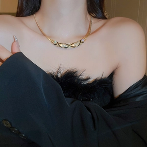 Close-up of a gold-plated curved necklace with black enamel stripes and shimmering crystals