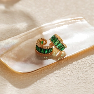 Macro detail of 18K gold plated C-shaped ear cuff with emerald green zircon stones
