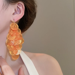 Close-up of orange multi-layered shell earrings on model with bohemian style