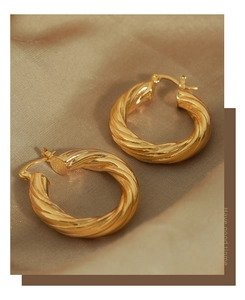 Macro view of gold twisted rope hoop earrings resting on champagne silk fabric background