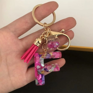 Detailed view of resin letter F keychain with pink sequins, golden hardware and tassel