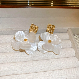 Macro shot of white flower earrings with pearl luster and golden textured studs in a jewelry box