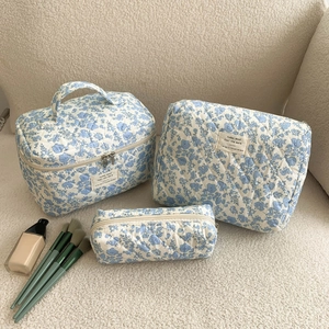 Three sizes of blue floral quilted cotton toiletry bags on a soft beige fabric background