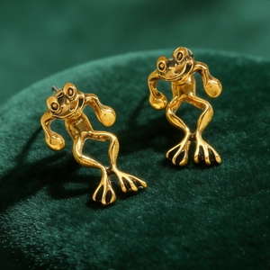 Macro shot of creative golden frog stud earrings on premium dark green velvet