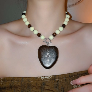 Gros plan d'un collier ethnique avec perles, cœur en bois sombre et pendentif croix