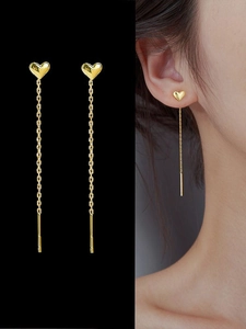 Macro detail of 18K gold heart tassel earrings showing metallic luster and model wear