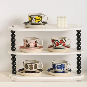 Three-tier white ceramic display rack featuring vintage hand-painted coffee cups and saucers