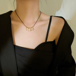 Gold LOVE letter pendant on black cord necklace worn by a model in black attire