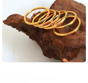 Close-up of five thin gold-plated rainbow zircon rings stacked on textured wood