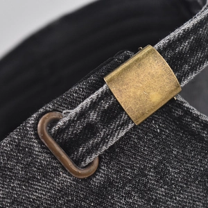 Macro shot of the adjustable vintage brass buckle on washed black denim baseball cap